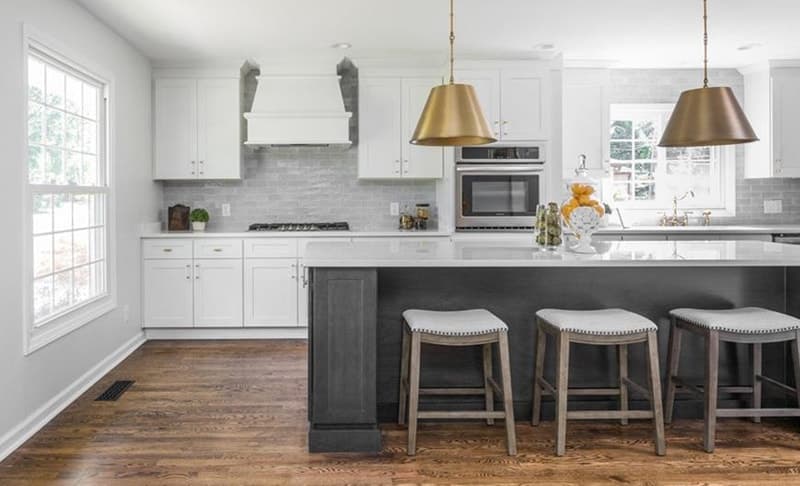 White shaker kitchen with a dark island, brass pendant lights, and wood floors