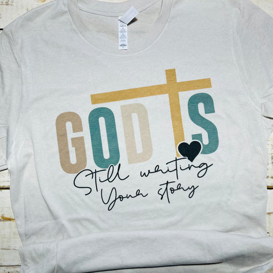 "Red Oak Faith Collection Cement T-shirt with 'God is Still Writing Your Story' design."