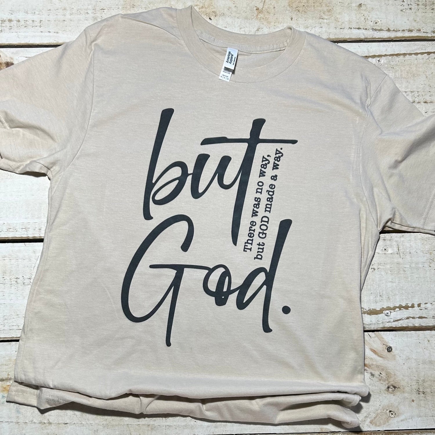 Alt Text: A bone-colored American Apparel T-Shirt from the "But God Made a Way" Red Oak Faith Collection, featuring an impactful message on the front. The shirt combines comfort and durability with a touch of sophistication, making it a versatile and stylish expression of faith.