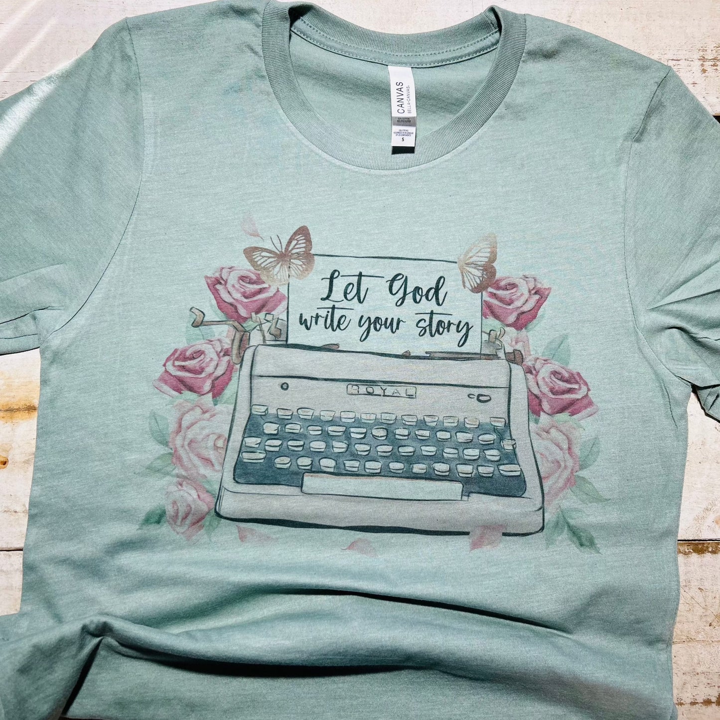 "Heather sage Bella-Canvas T-Shirt from Red Oak Faith Collection featuring 'Let God Write Your Story' in elegant font – a blend of comfort, style, and spirituality."