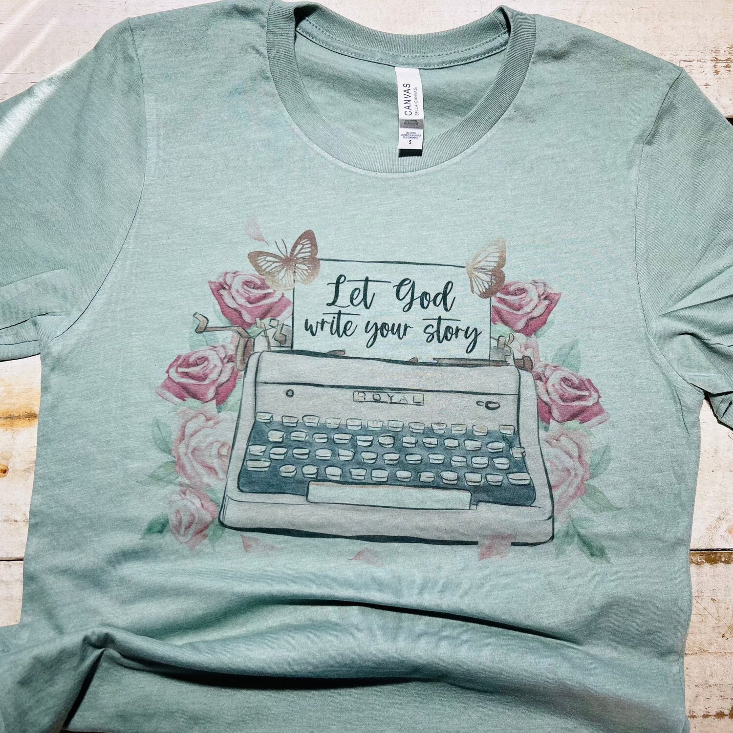 "Heather sage Bella-Canvas T-Shirt from Red Oak Faith Collection featuring 'Let God Write Your Story' in elegant font – a blend of comfort, style, and spirituality."