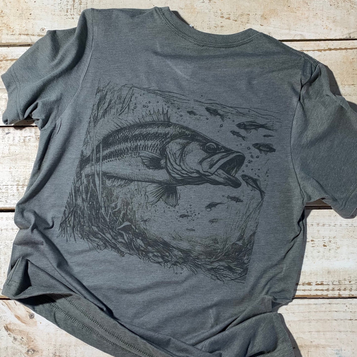 Alt text for an image of the “Largemouth Bass” Backyard to Backwoods Shirt:  “A stylish t-shirt featuring a largemouth bass design in its natural habitat, surrounded by lush greenery. Perfect for fishing enthusiasts and nature lovers.” Back of shirt.