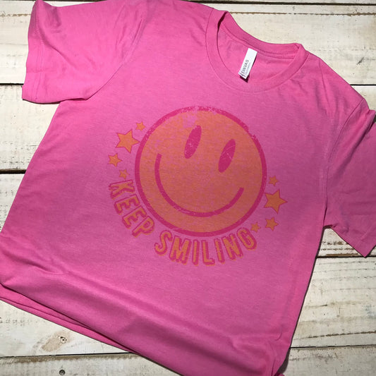 A Bella Canvas Charity Pink shirt with the words "Keep Smiling" printed in a playful and vibrant font. The design is centered on the shirt, creating a visually pleasing contrast against the pink background. Not Bleached Teacher Shirt, Shirt for Teacher