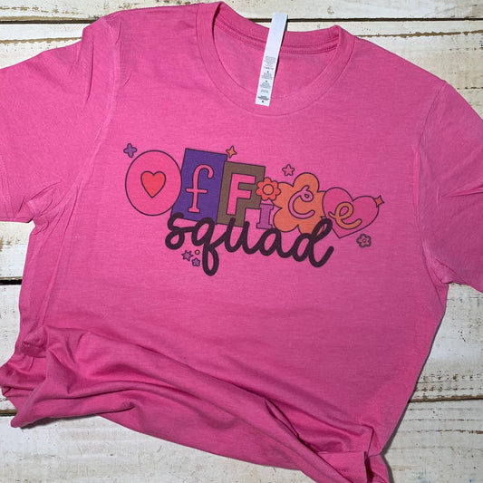 **Alt Text for "Office Squad" Teacher Shirt Image:**  A cheerful teacher wearing a "Office Squad" teacher shirt in a vibrant Heather Charity Pink color. The shirt features a stylish and playful design with the words "Office Squad" in a bold font. The teacher smiles, standing confidently, ready to take on the day with a dash of school spirit.