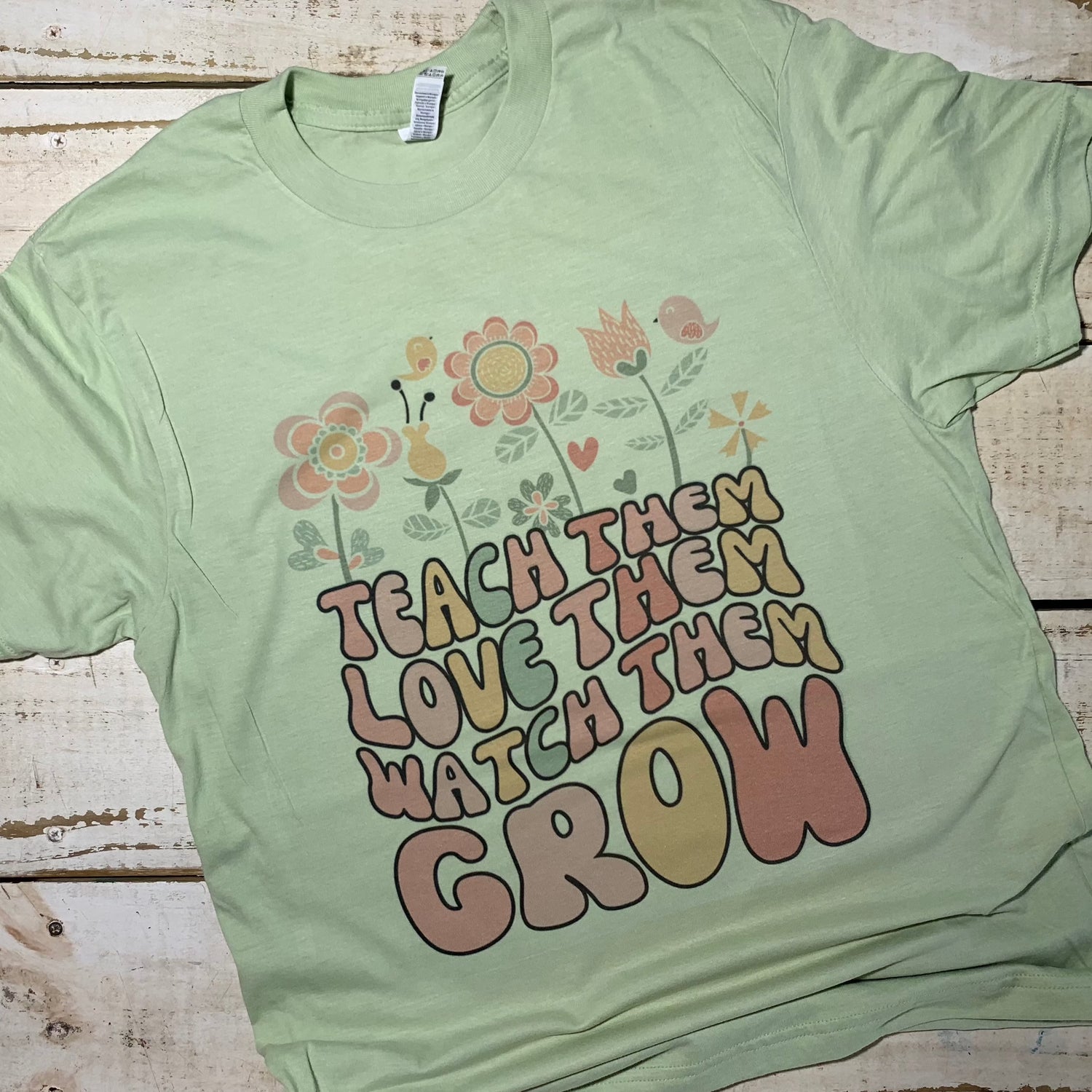 The Teach Them Love Them Watch Them Grow Teacher Shirt printed on an American Apparel Cucumber t-shirt is part of the Red Oak Teacher Shirt collection.