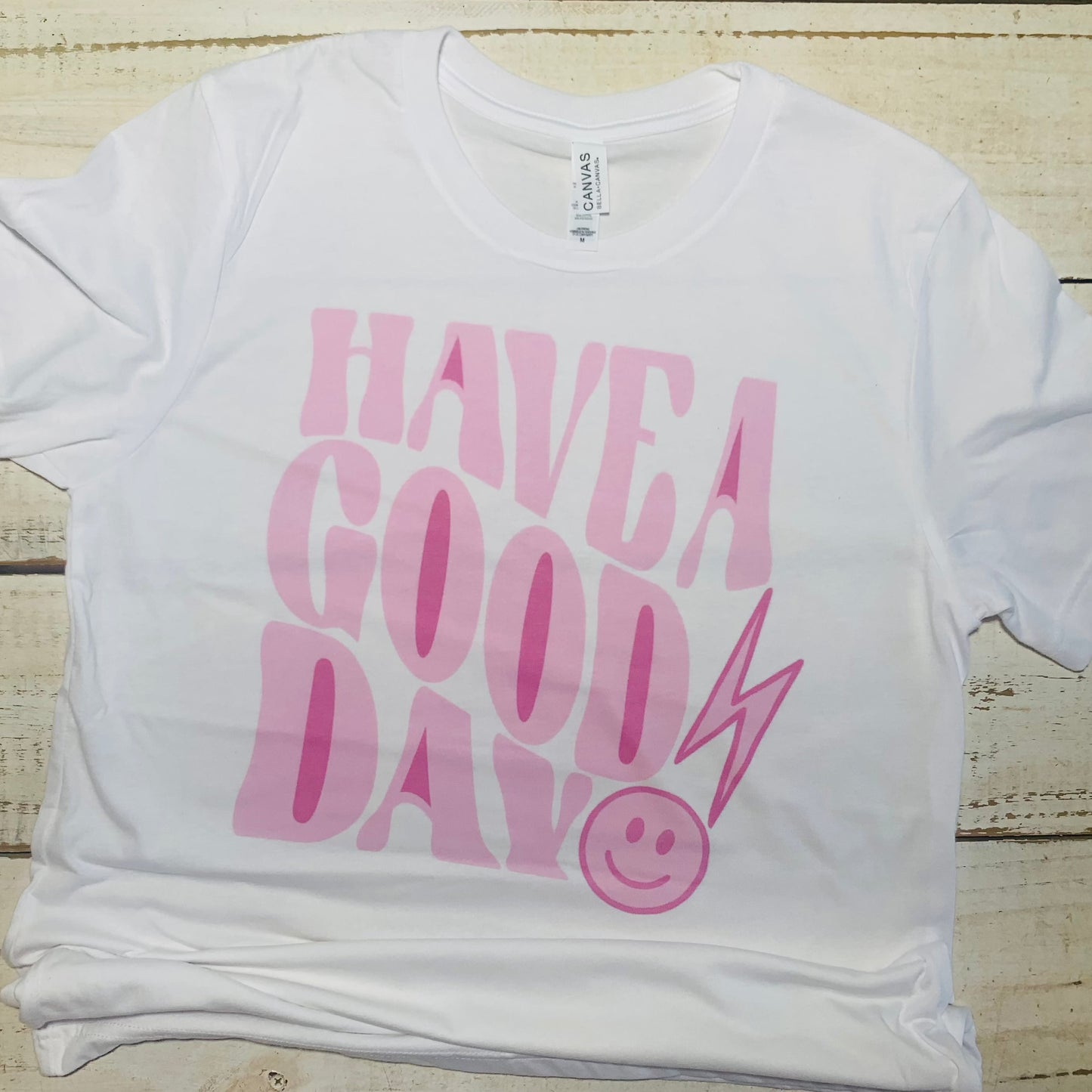 **Alt Text for "Have a Good Day" Teacher Shirt Image:**  A close-up view of a Bella-Canvas White teacher shirt with the words "Have a Good Day" printed in bold, friendly letters. The shirt is neatly folded, showcasing its high-quality fabric and timeless design.