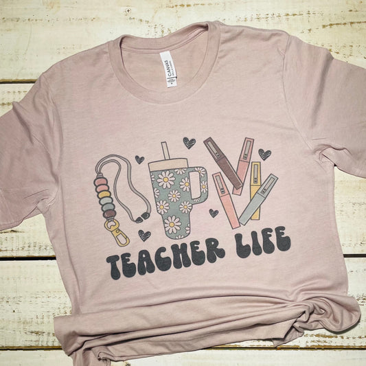 Alt Text for "Teacher Life" Shirt Image:  "Teacher Life" shirt on a Bella Canvas Heather Pink Gravel background. The shirt features a playful design that includes school supplies like pencils, apples, and books, along with the text "Teacher Life" in a cheerful font. The pink color of the shirt complements the design and adds a touch of vibrancy. The shirt is a comfortable and stylish choice for teachers to express their passion for education.