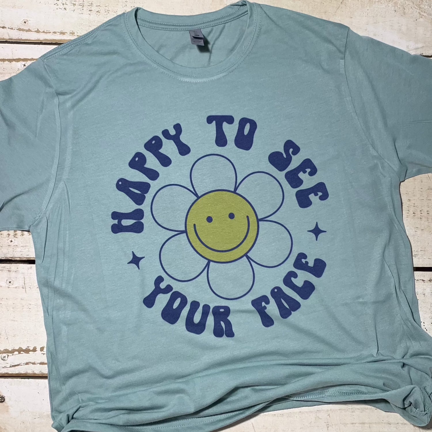 **Alt Text for "Happy To See Your Face" Teacher Shirt:**  "Happy To See Your Face" Teacher Shirt displayed on a Next Level Stonewash Green shirt. The design features a heartwarming message surrounded by vibrant colors, reflecting positivity and dedication to teaching. The shirt exudes comfort and style, making it suitable for both classroom and casual wear. It embodies the spirit of education and the joy of connecting with students through smiles and positivity.  Shirt for Teacher