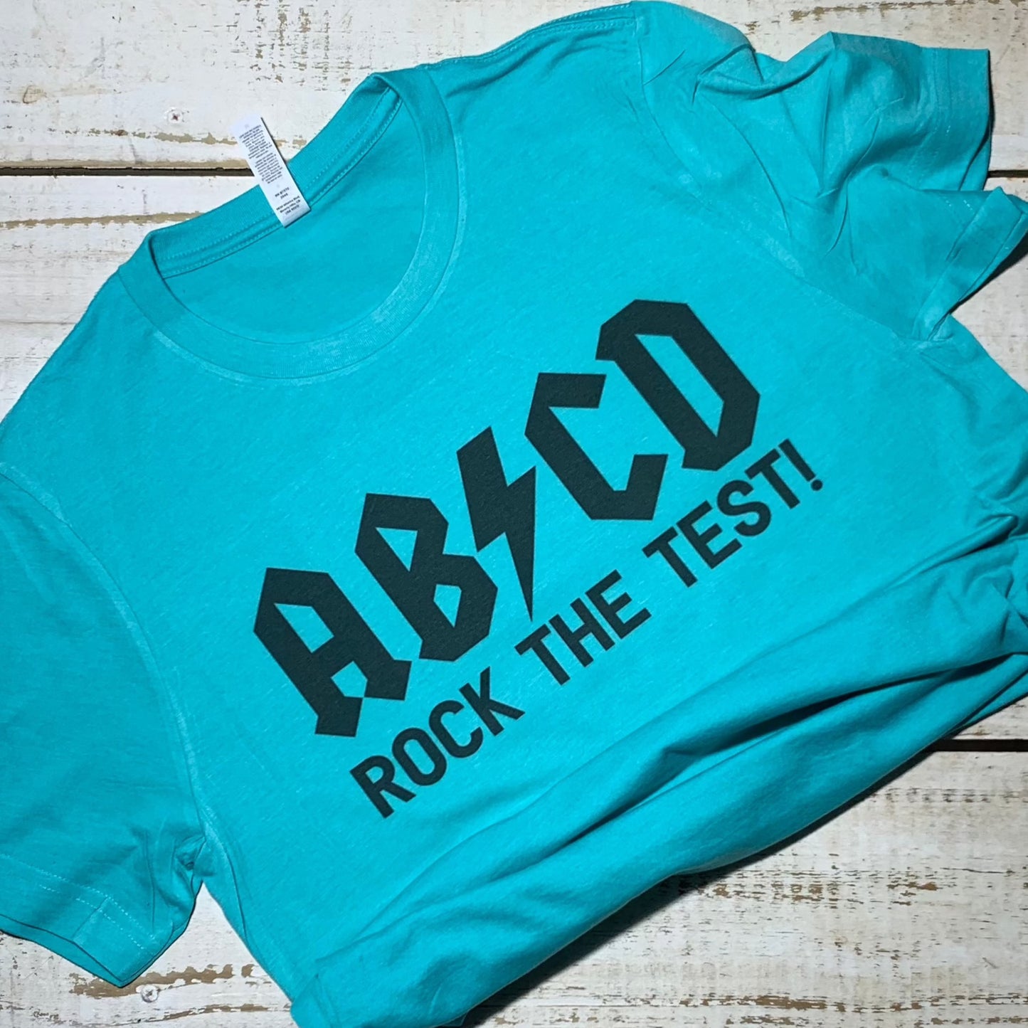 👕 **Teacher Shirt Alt Text** 👕  "ABCD Rock The Test" - A vibrant neon blue poly/cotton shirt for teachers of all grades. The shirt features an ABC-inspired design that reads "ABCD Rock The Test" in bold, playful letters. It's the perfect blend of style and comfort for educators, encouraging confidence in and out of the classroom. #TeacherShirt #ShirtsForTeachers