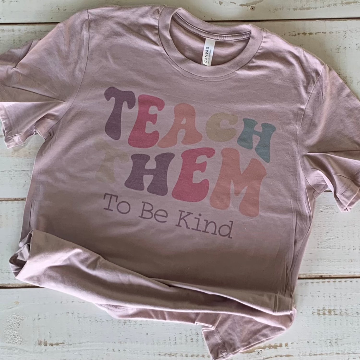 "Bella-Canvas pink gravel Teacher Shirt with 'Teach Them To Be Kind' message - a comfy and stylish statement for educators with a passion for shaping young minds."