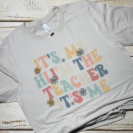 **Alt Text for Teacher Shirt Image:**  "Teacher shirt in silver color with the playful text 'It’s Me, Hi, I’m the Teacher, It’s Me' in bold, whimsical font. The shirt is made of soft and comfortable poly/cotton fabric and is suitable for teachers of all grades. A must-have for educators who want to showcase their pride and style in and out of the classroom."