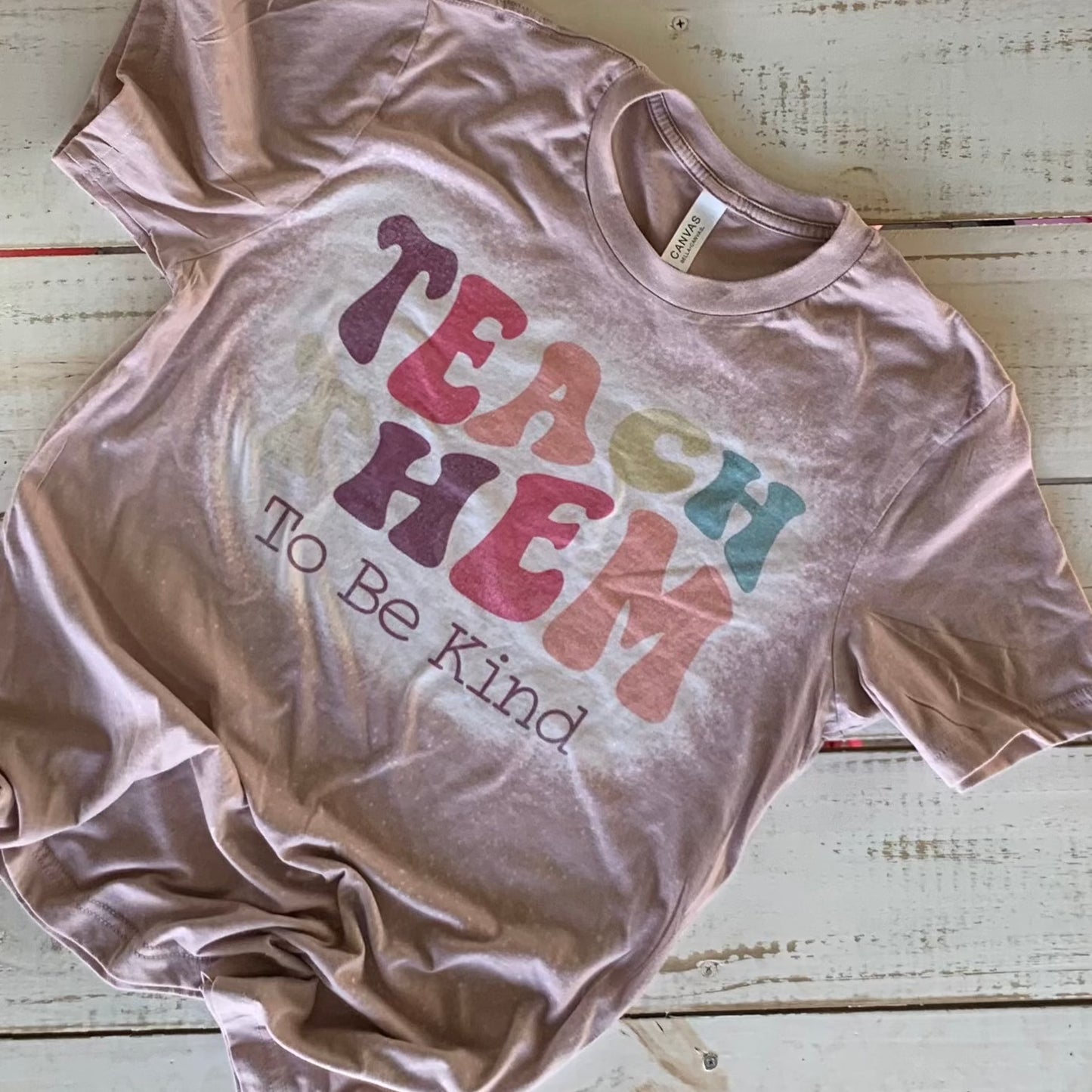 "Bella-Canvas pink gravel Teacher Shirt with 'Teach Them To Be Kind' message - a comfy and stylish statement for educators with a passion for shaping young minds." Bleached