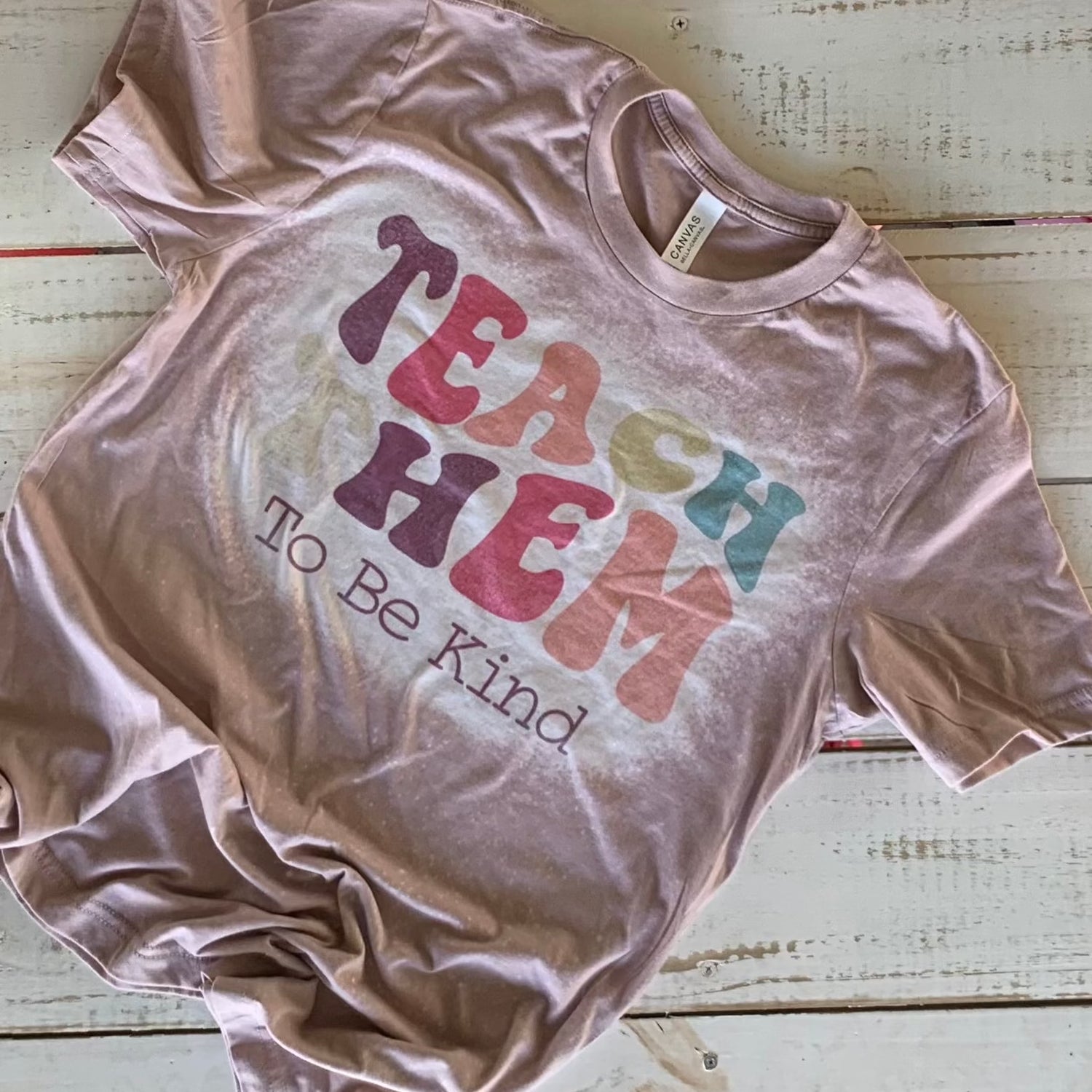 "Bella-Canvas pink gravel Teacher Shirt with 'Teach Them To Be Kind' message - a comfy and stylish statement for educators with a passion for shaping young minds." Bleached